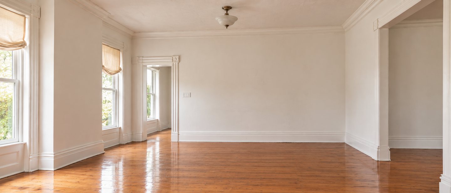 The dining room before: an empty white room with a single pendant light, roman shades and pine floors.